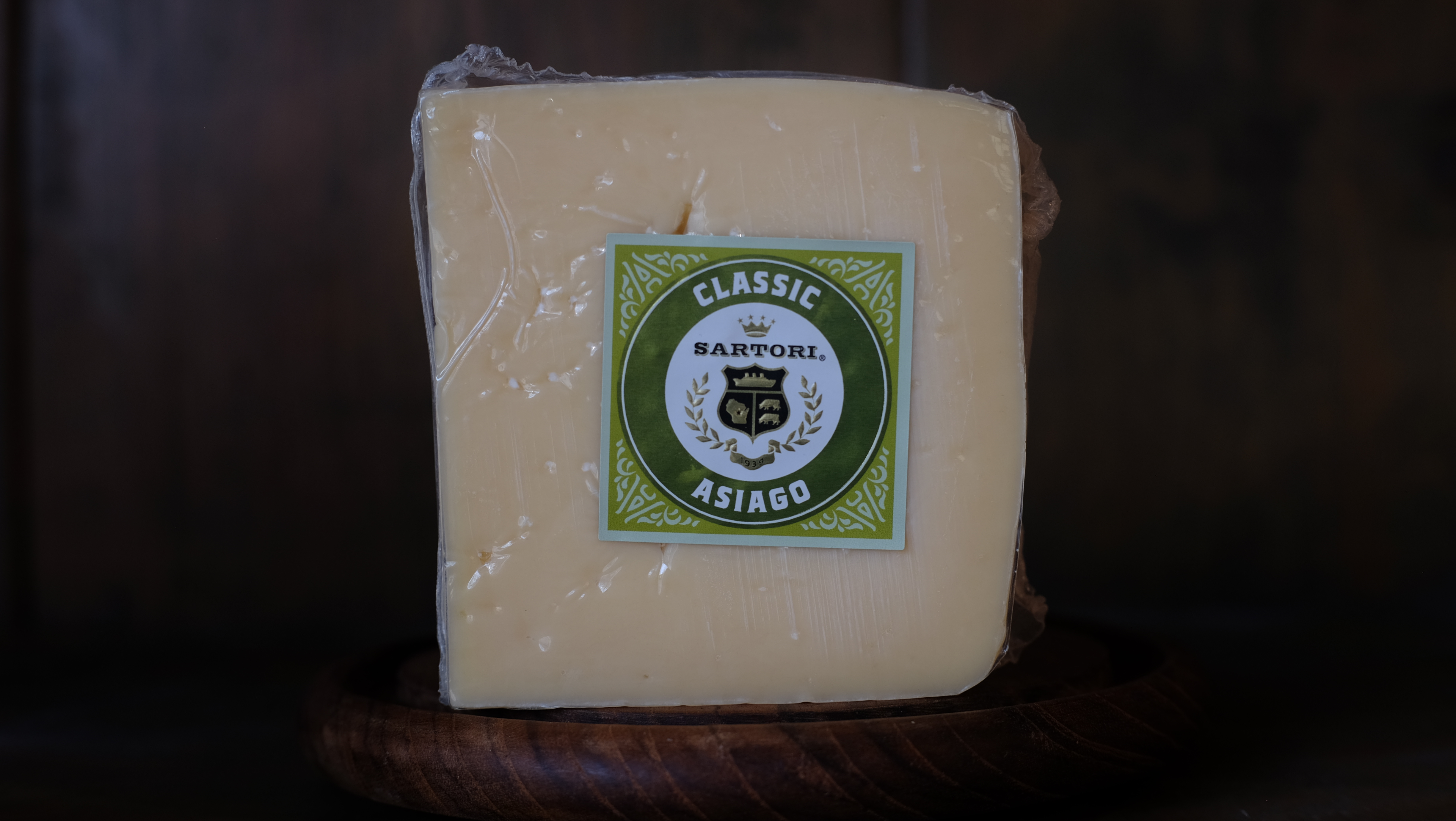 Wedge of aged Asiago cheese on a wood cutting board